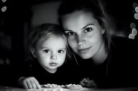Adult woman of Caucasian ethnicity and young child, approximately 2-4 years old, posing together in black and white portrait. Mother and daughter share intimate moment while enjoying popcorn, expressing love and family bonding.