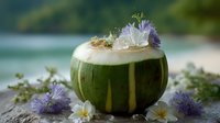 Tropical coconut cocktail garnished with fresh plumeria and purple flowers served on stone surface against blurred beach background, summer refreshment.