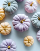 Pastel colored pumpkins in pink, blue and peach tones arranged on light gray background. Modern festive autumn composition with painted decorative gourds.