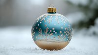 Elegant blue and gold Christmas ornament with delicate snowflake pattern resting in fresh snow, creating festive winter holiday atmosphere with soft bokeh background.