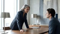 Professional mature businesswoman mentoring young male colleague in modern office conference room during corporate meeting.