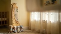Cozy nursery room with cute giraffe wall decal, white crib, soft toys and warm sunlight streaming through window creating peaceful atmosphere.