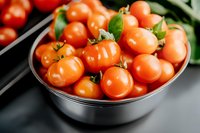 Fresh ripe cherry tomatoes in metal bowl, close up view of organic red tomatoes with green stems, healthy vegetarian ingredients for cooking.