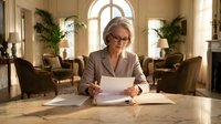 Professional mature businesswoman with glasses reviewing documents at elegant office desk in luxury corporate interior with arched windows and plants.