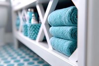 Neatly folded turquoise towels stacked on white bathroom shelving unit with organized storage compartments and decorative accessories in modern spa interior.
