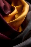 Elegant waves of luxurious silk fabric in burgundy, golden yellow and charcoal gray colors create dramatic folds and shadows against dark background.