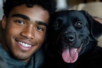 Young African American man and black Labrador dog sharing joyful moment together, both with bright smiles and happy expressions in close-up portrait.