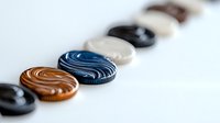 Colorful round buttons arranged in diagonal line on white background showcase swirled patterns and varied textures, suitable for fashion and craft designs.