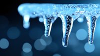 Frozen icicles with air bubbles hanging against blurred blue bokeh background create dramatic winter atmosphere and cold weather concept.