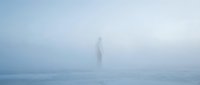 Solitary figure standing in dense fog on empty beach at dawn, creating atmospheric and moody scene for editorial and conceptual projects.
