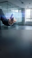 Businessman in suit touching glowing virtual business button in modern office, digital technology concept for corporate presentations.