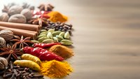 Colorful aromatic spices and herbs arranged on wooden surface including turmeric, paprika, cinnamon sticks, star anise, cardamom pods for cooking and seasoning.