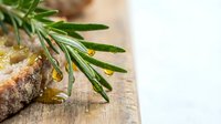 Fresh rosemary herb sprig with olive oil drops on rustic wooden cutting board. Natural cooking ingredient for Mediterranean cuisine and culinary preparations.