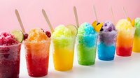 Colorful shaved ice drinks with wooden spoons arranged in a row on pink and white background, perfect for summer beverage, dessert, and refreshment concepts.