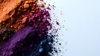 Colorful cosmetic powder explosion with orange pink purple and blue makeup pigments scattered on white background for beauty and fashion projects.
