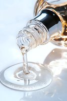 Clear liquid pouring from bottle into wine glass on white background, creating elegant stream with light reflections and shadows in minimalist composition.
