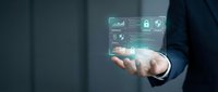 Businessman holding holographic digital interface with data analytics charts and security icons floating above palm in modern corporate environment.