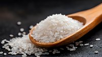 White rice grains in wooden spoon on dark surface for cooking and nutrition concepts.
