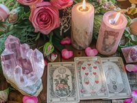Pink roses and lit candles surrounding tarot cards with crystal clusters and scattered heart petals create mystical divination altar setting for spiritual readings.