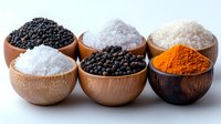 Variety of colorful spices and seasonings in wooden bowls including black peppercorns, sea salt, turmeric powder arranged in two rows on white background.