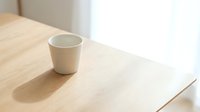 Empty white ceramic mug on light wooden table with natural sunlight, minimalist workspace setup for beverage, coffee, tea, or product mockup designs.