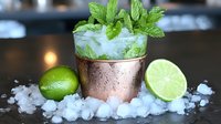 Fresh mojito cocktail in copper mug garnished with mint leaves and lime, served on crushed ice, close-up view against dark background. Perfect for beverage menu.