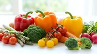 Fresh colorful vegetables including bell peppers, broccoli, tomatoes, asparagus and radishes arranged on white surface for healthy cooking and nutrition.