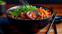 Grilled chicken teriyaki bowl with glazed meat, fresh scallions, and julienned carrots served in black ceramic bowl on wooden table, moody restaurant lighting.