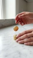 Person with fair skin applying amber-colored gel or serum from a gold-trimmed jar onto marble surface near window with natural light, demonstrating skincare product application and cosmetic beauty routine.