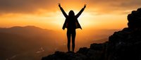 Silhouette of victorious hiker with raised arms celebrating success on mountain peak at golden sunset with dramatic sky and valley landscape below.