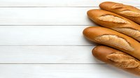 Fresh crusty French baguettes on white wooden background with copy space. Traditional artisanal bread loaves arranged in corner composition.
