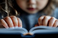 Close up view of small hands holding open book pages against blurred background, creating atmospheric educational scene with soft natural lighting.
