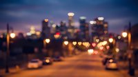 Blurred city skyline at dusk with bokeh lights from traffic and buildings creating romantic heart-shaped illumination effects on urban street.