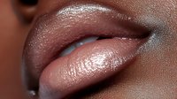 Close up of plump glossy lips with nude pink lipstick on dark skin, showing moisturized texture and natural shine in macro photography detail.