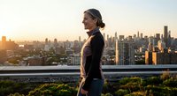 Professional businesswoman in athletic wear standing on urban rooftop terrace overlooking city skyline at golden hour sunset for wellness and work-life balance.