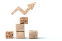 Wooden blocks arranged as steps with rising arrow symbol on white background, representing business growth, success and progress in finance markets.