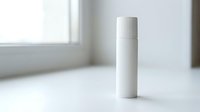 White minimalist cosmetic bottle mockup on clean surface near window, blank label ready for branding, skincare packaging design concept.