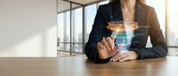 Businesswoman in dark blazer holding transparent tablet with holographic data visualization and digital interface display in modern office workspace.