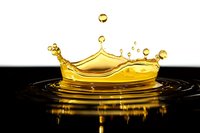 Golden liquid crown splash with droplets frozen in motion against black background, creating mirror reflection on surface. Dynamic fluid photography.