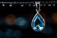 Elegant teardrop aquamarine pendant necklace with silver setting against dark background with water drops and bokeh lights creating luxurious jewelry atmosphere.