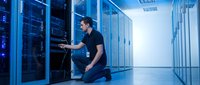 IT technician maintaining server equipment in modern data center with blue LED lighting for technology and network infrastructure solutions.