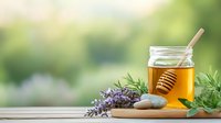 Golden honey jar with wooden dipper on rustic wooden table, fresh lavender flowers and zen stones against blurred garden background. Natural wellness concept.