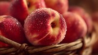 Fresh ripe peaches with water droplets in rustic wicker basket, macro view showing juicy texture for food photography and harvest themes.