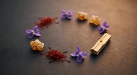 Natural spices saffron threads turmeric powder violet flowers wooden clothespin arranged in circle on dark textured surface for culinary cooking ingredients.