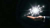 Businessperson holding glowing light burst in palm against dark background, representing innovation, success, and creative solutions for corporate and entrepreneurial concepts.