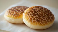 Two golden tiger bread rolls with distinctive cracked pattern crust on white plate, fresh baked artisan bakery goods for breakfast or sandwich making.