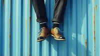 Businessman legs in brown leather shoes and dark suit pants against blue corrugated metal wall background for corporate and professional concepts.
