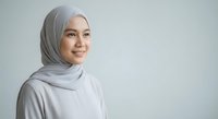 Smiling young Southeast Asian Muslim woman in gray hijab on light background, copy space, confident and friendly expression.