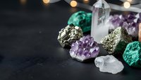 Collection of healing crystals and gemstones including amethyst, quartz, malachite and pyrite arranged on dark surface with warm bokeh lights.
