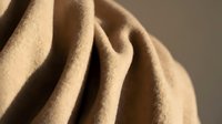 Beige wool fabric with soft folds and drapes, showcasing natural texture and material quality for fashion, textile, and design projects.